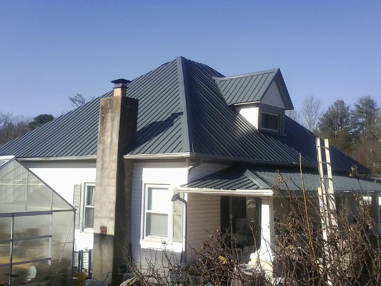 Dark blue standing seam metal roof on a white farmhouse with dormer — Slate & Tile Roof Repair by Roofing Brothers in Melvern
