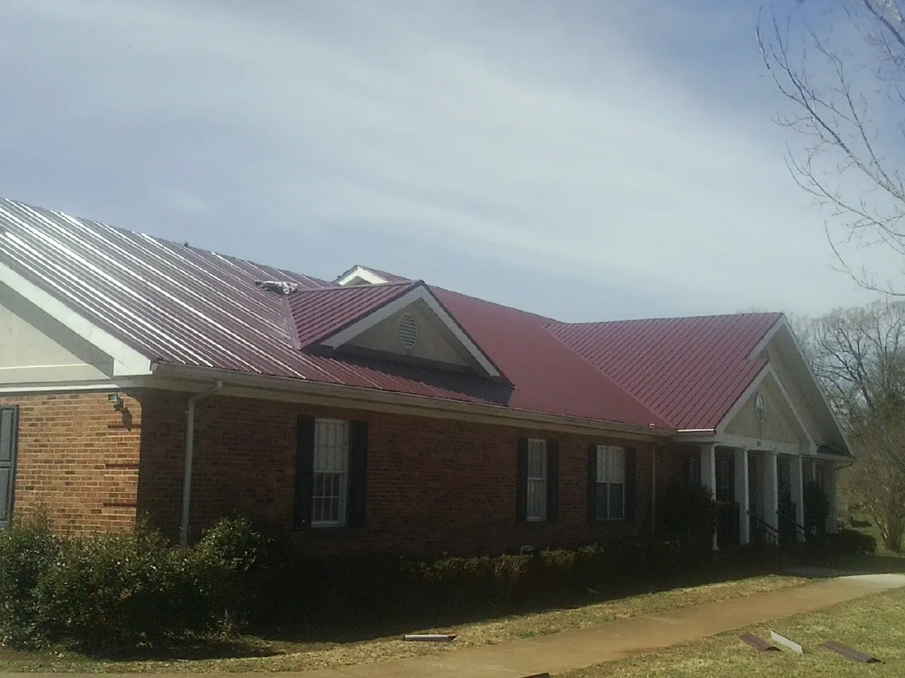 Red metal roof with gabled entries on a long brick building, from a Hail Damage Roof Repair job in Melvern