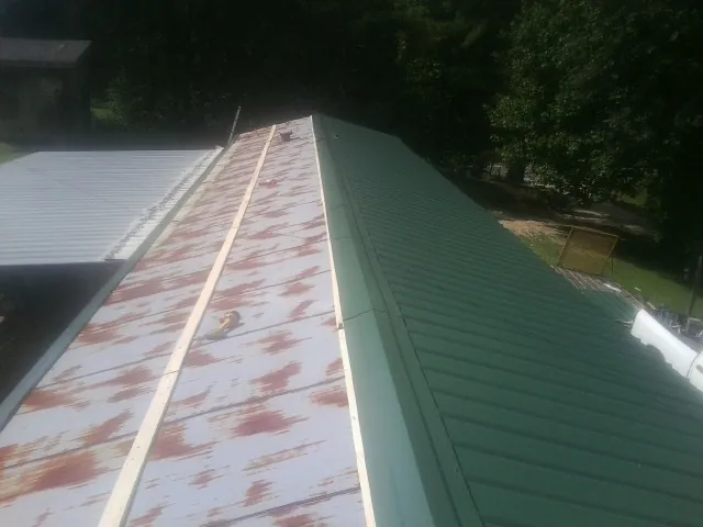Old rusted panels beside newly installed green metal roofing — Wind Damage Roof Repair by Roofing Brothers in Melvern