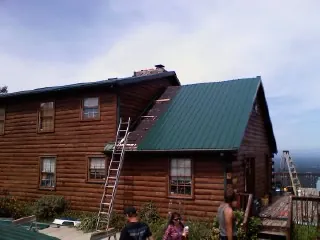 Green metal roof going on a two story log home with ladders set in Melvern