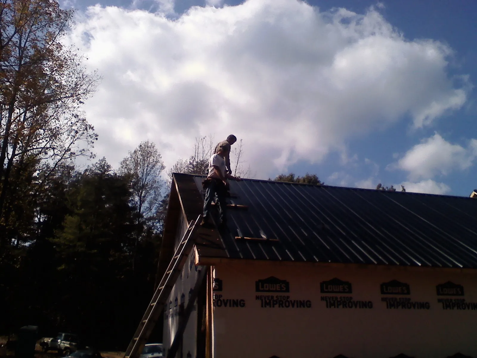 Roofer fastening dark metal panels high against a cloudy sky, from a Roof Inspection job in Melvern
