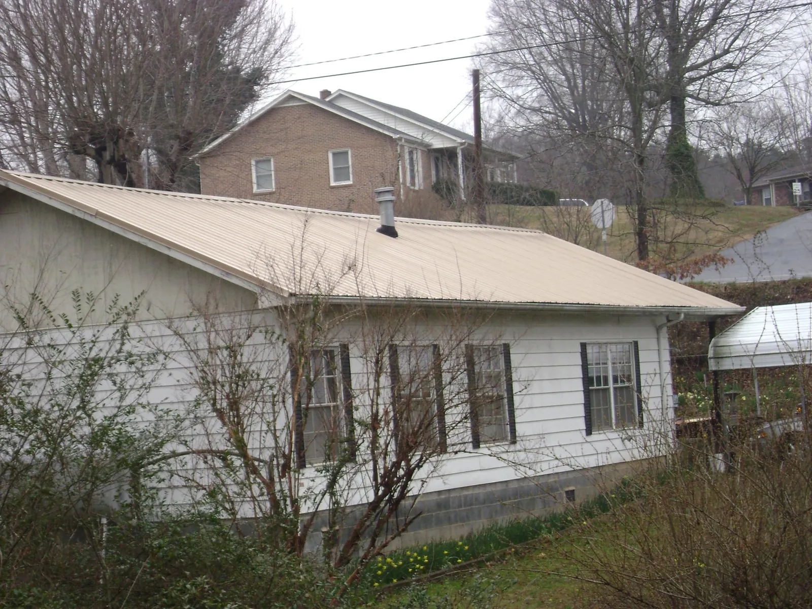 Tan metal roof on a white sided house set into a hillside — Commercial Roofing by Roofing Brothers in Melvern