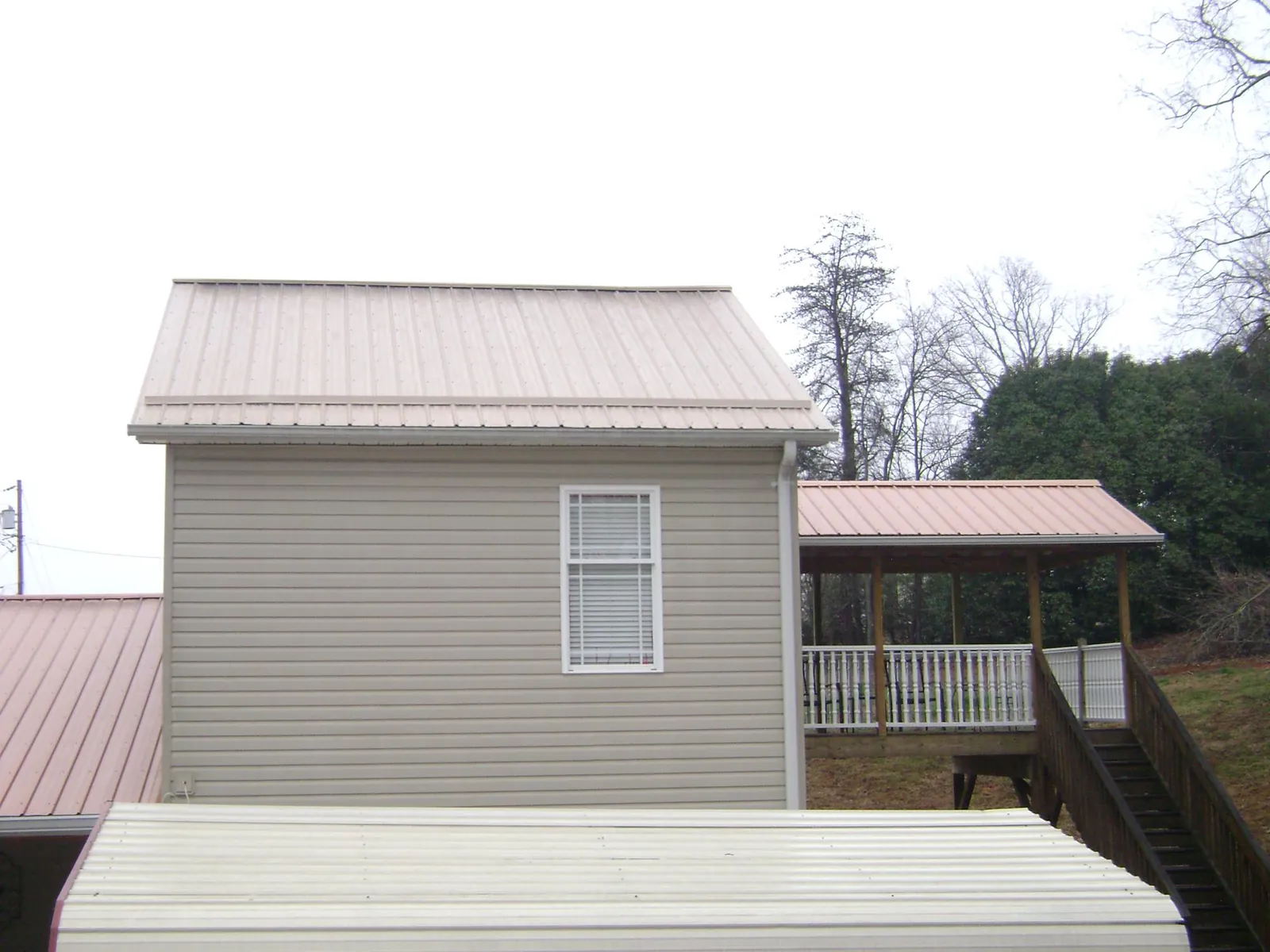 Tan metal roofs on a two story addition and attached porch, from a Roof Replacement job in Melvern